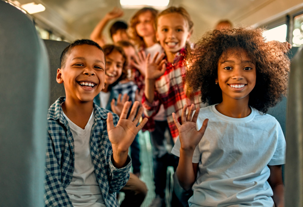Students smiling and waving while riding a school bus